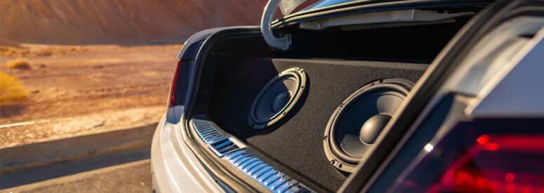 A car in a desert with its trunk open and a speaker system installed therein