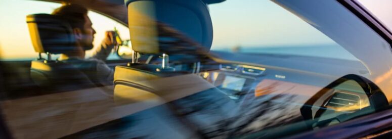 A view of a man driving a car on a road through the passenger side window